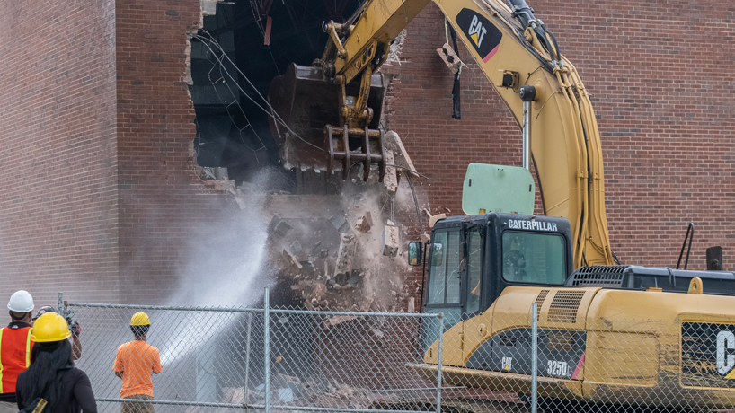 A backhoe starts demolition on the JC Penney Auditorium as members of Hillsdale Demolition look on