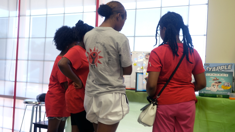 Four students, Black middle school aged girls, have their back turned as they inspect a display