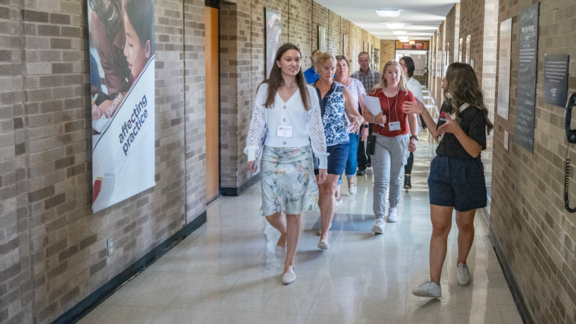 An optometry student, white woman in black t-shirt, leads a tour of about seven people through the halls of the College of Optometry