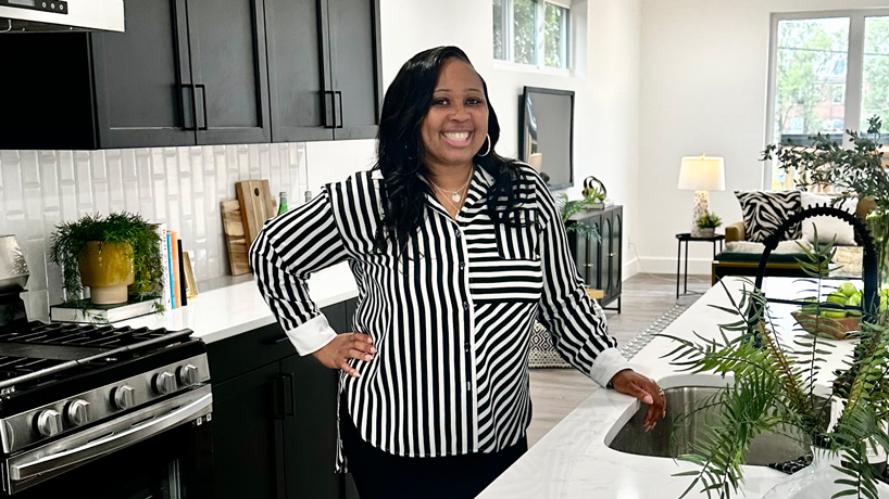 Janelle Stowers, black woman in black and white striped top, stands in kitchen with white marble countertops
