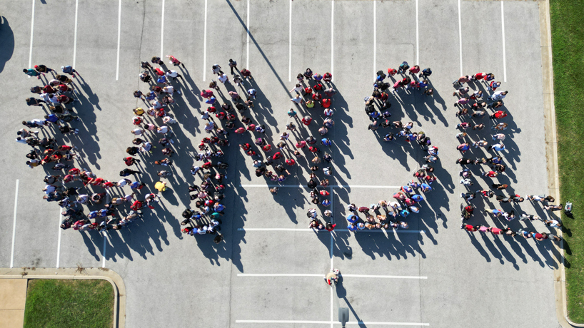 An overhead drone photo shows new students using their bodies to spell UMSL on the parking lot outside of the Millennium Student Center. 