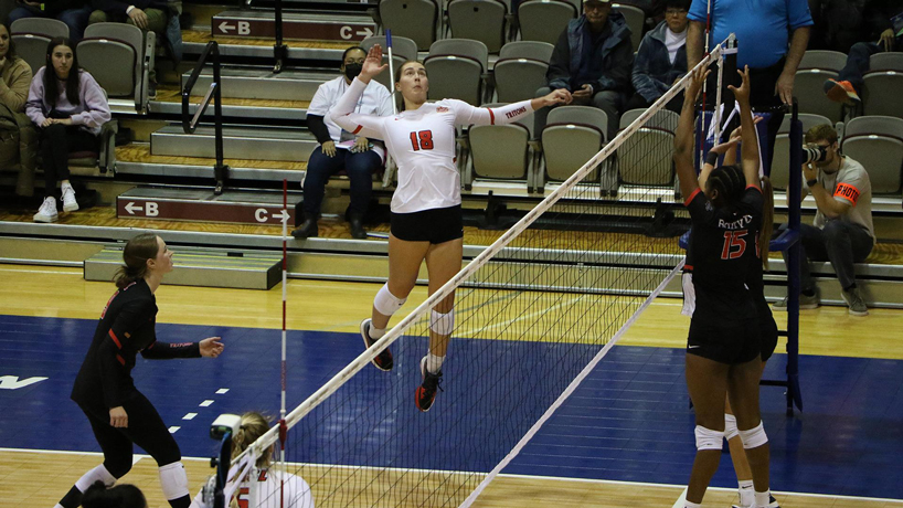 Lexie Rang leaps in the air and waits to hit a volleyball as a defender sets up a block