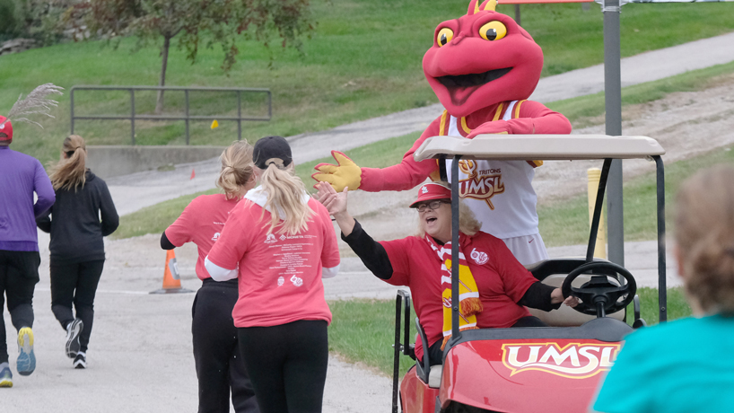 Chancellor Kristin Sobolik and Louie the Triton high-five runners from their golf cart during the UMSL Alumni Association 5K Run/Walk