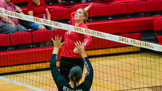 Volleyball player Delaney Humm prepares to swing at a ball while leaping above the net as a defender lifts her arms to try to block