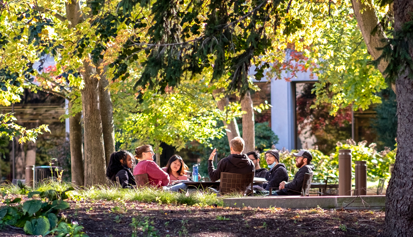 A group of students sit in a circle to hold a class discussion in the Quad on a fall day