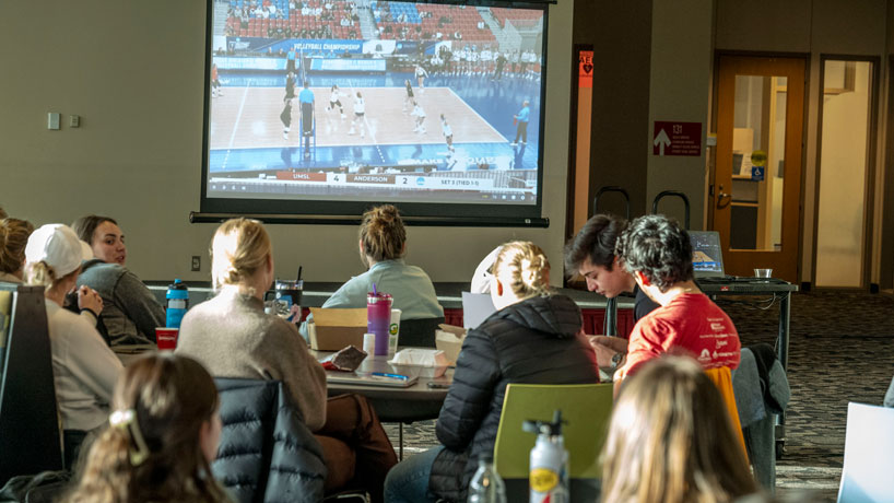 Students watch the NCAA Division II volleyball tournament on a projector screen in The Nosh