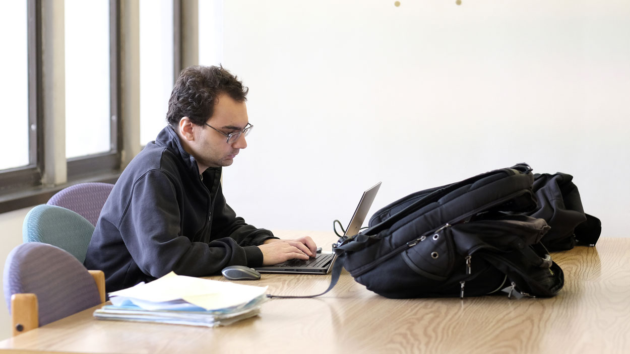 A male student sits in front of a computer doing coursework