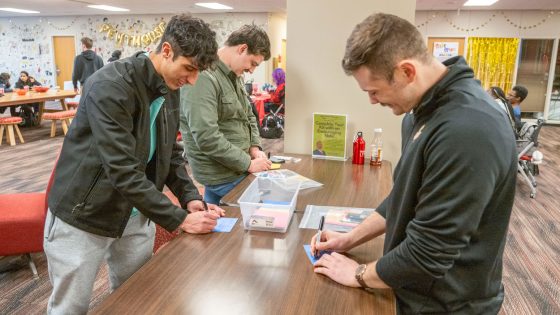 Freshman finance major Zaid Fares, junior information systems major Alex Skinker and admissions staff member Sean Marshall write notes of encouragement to be placed in new mom kits.