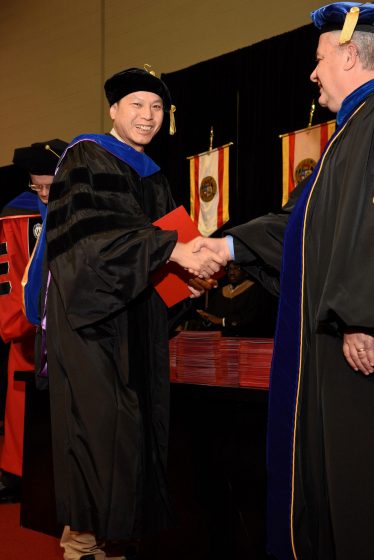Yiuman Tse shakes hands with Provost Steven J. Berberich during his walk across the commencement stage