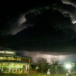 Lightning flashes from behind a storm cloud moving east of the Millennium Student Center at night