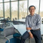Assistant Professor Lei (Jeremy) Xu sitting on the edge of a table in an empty classroom
