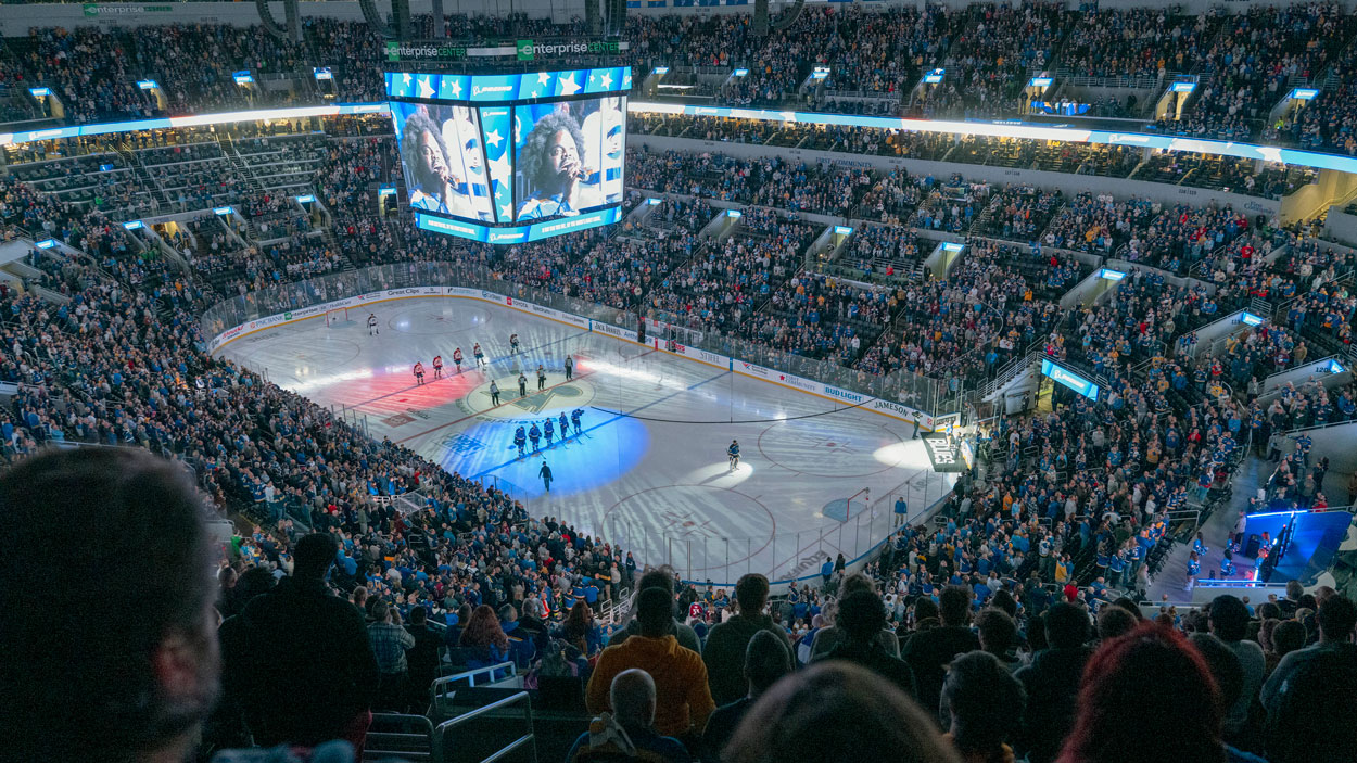 The lights dim and the crowd stands at the Enterprise Center during the playing of the national anthem during UMSL Night at the St. Louis Blues