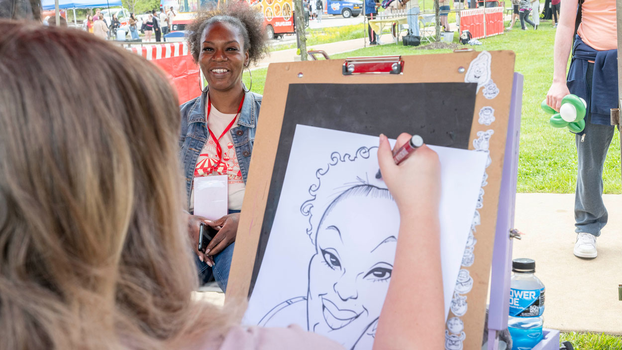 Eboni Alexander, a senior office support assistant in the Office of Health, Counseling and Disability Access Services, sits to get her caricature made.