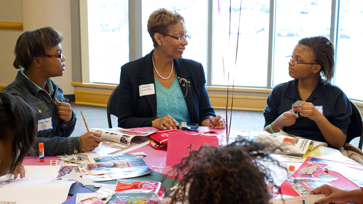 Retired Judge Brenda Stith Loftin works with a table full of middle school girls and a teacher at the 2014 Girls Summit held on the UMSL campus.