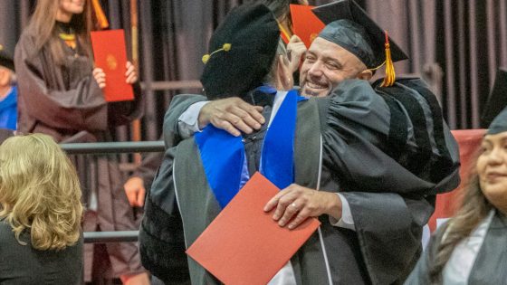 Teaching Professor Lynn Staley hugs UMSL teaching professor, Lynn Staley hugs studio art graduate Bob Madden after he receives his diploma.