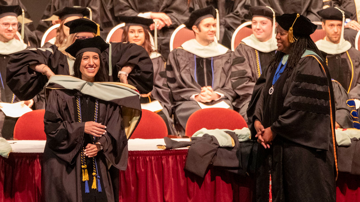 Dr. Kathleen Boland hoods new College of Optometry graduate Dr. Samantha Knoblauch and Dean Dr. Keshia Elder looks on during Friday's ceremony for the College of Optometry
