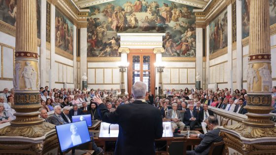 An image taken from behind Michael Cosmopoulos as he delivers a lecture in the main hall of the Academy of Athens