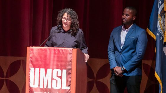 Current student Abby Wall speaks from a lectern on stage as fellow student Devin Womack looks on