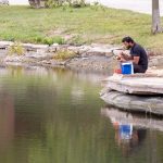 Cybersecurity graduate student Dipak Sunar eats lunch on the edge of the ponds outside of the Millennium Student Center