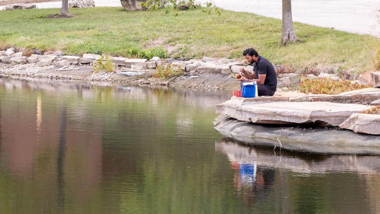 Cybersecurity graduate student Dipak Sunar eats lunch on the edge of the ponds outside of the Millennium Student Center