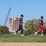 A crane takes a wrecking ball to the Social Sciences and Business Building Tower Saturday morning on North Campus at the University of Missouri–St. Louis as a group of students runs in the foreground along Grobman Drive while taking part in the fourth annual UMSL Alumni Association 5K Run/Walk.