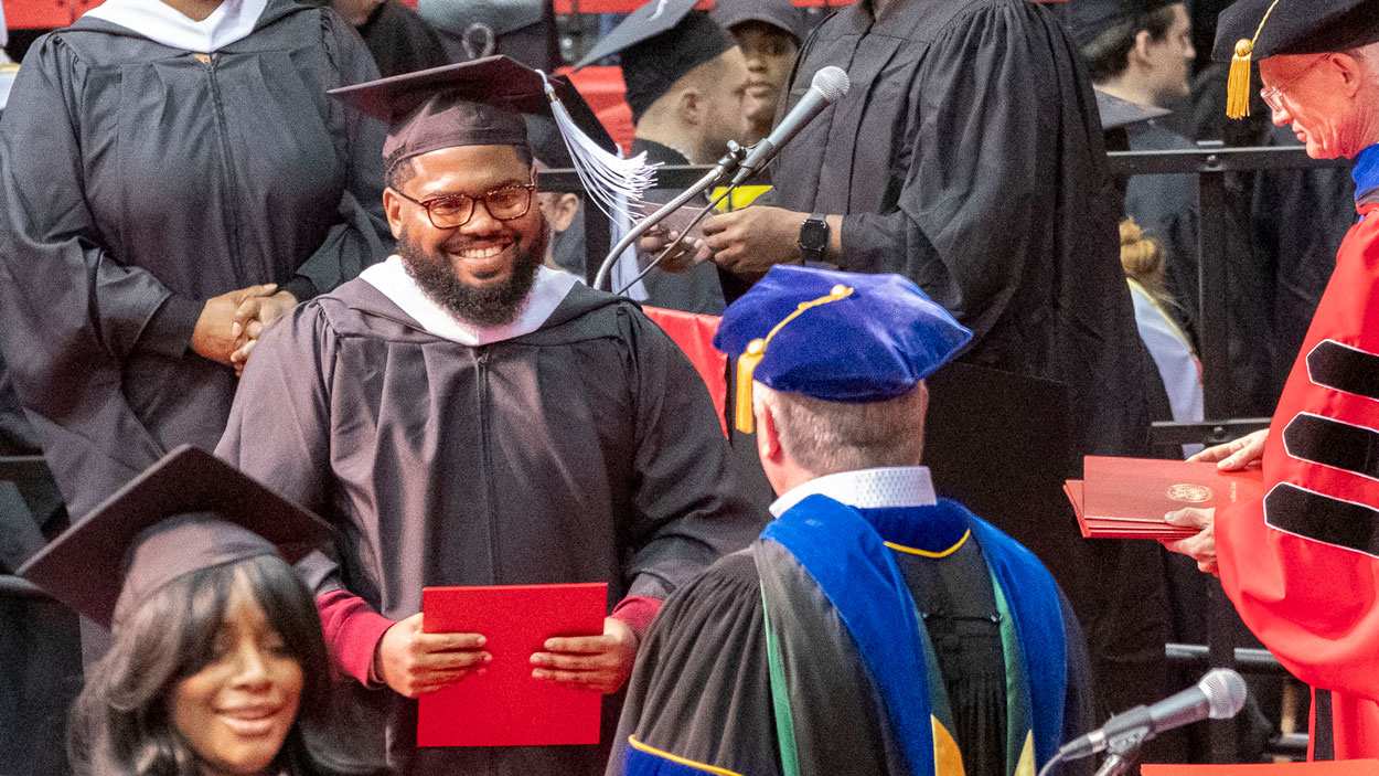 Communication graduate Austin Davis smiles as he walks across the commencement stage