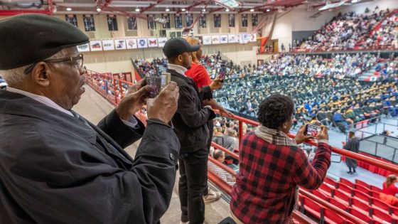 Family members stand to take pictures of their graduates as they walk across the commencement stage.