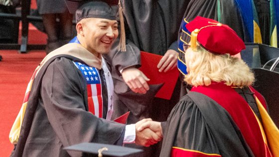 Accounting graduate Gregory Harmon shakes hands with Chancellor Kristin Sobolik as he crosses the commencement stage.