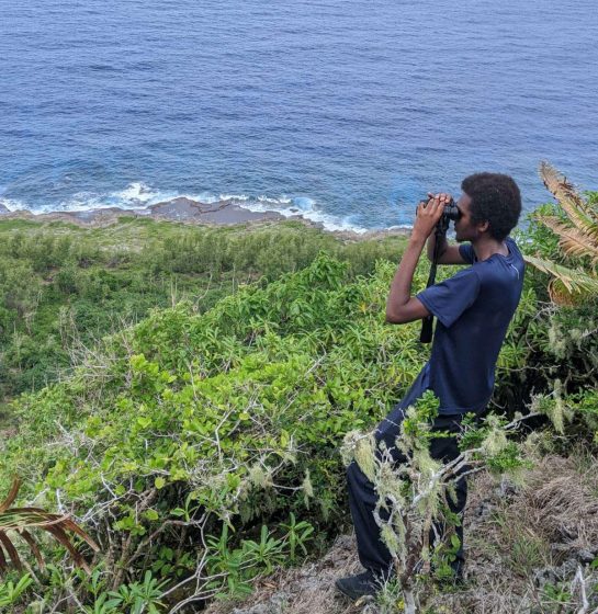 Kordell Hamilton peers through binoculars at the landscape in the Northern Mariana Islands