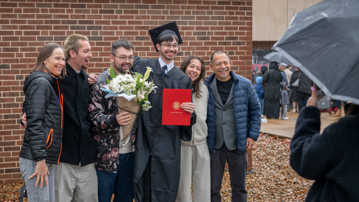 A new graduate takes photos in the rain with family and friends after Saturday's ceremony