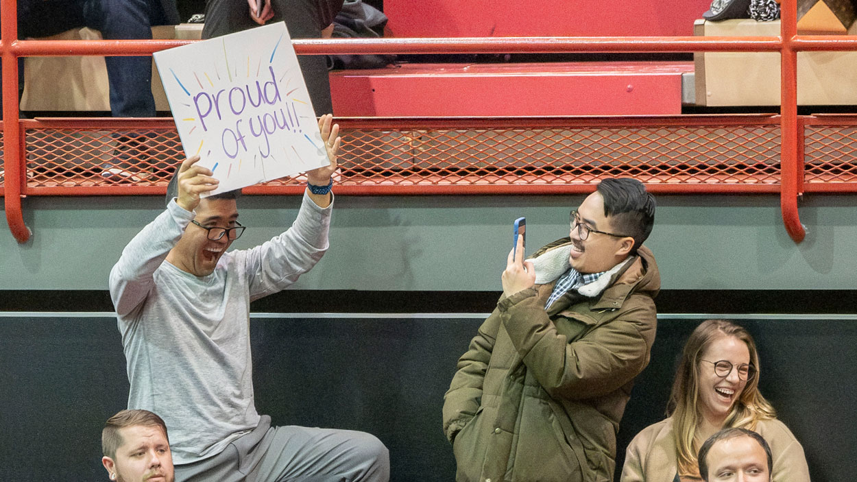 A family member holds up a sign that reads "Proud of you" 