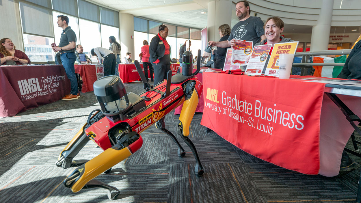 UMSL's newly renamed agile mobile robotic dog, Titan, visits the UMSL Graduate Business table and meets a few smiling faces at last week's Spring Involvement Jamboree in the Millennium Student Center as it showed off its new look