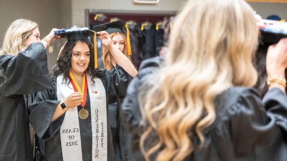 Nursing graduate Miranda Martin gets assistance with her mortarboard before the start of Saturday morning's commencement ceremony