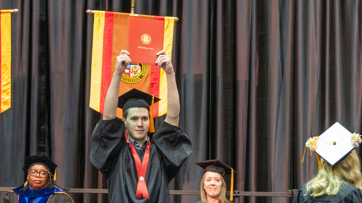 Nursing graduate Spencer Goodson holds up his diploma case after walking across the commencement stage