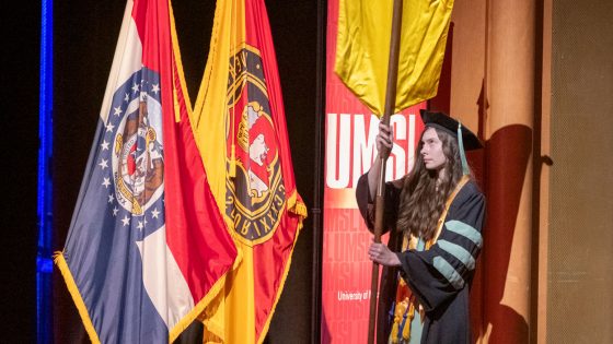Dr. Carly Poskochil, outstanding student in optometry, carries the College of Optometry's banner during the commencement ceremony