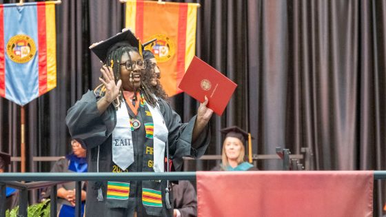 New chemistry graduate Zahria Patrick holds up her diploma cover as she exits the commencement stage