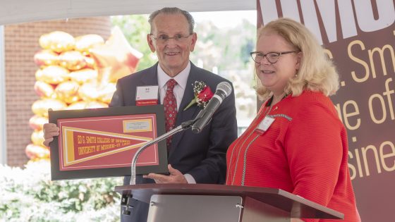 University of Missouri–St. Louis Chancellor Kristin Sobolik presents Ed G. Smith with a framed Ed G. Smith College of Business pennant during a dedication ceremony for the Ed G. Smith College of Business.