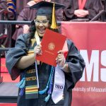 A nursing graduate holds up her diploma while wearing a TRIO sash