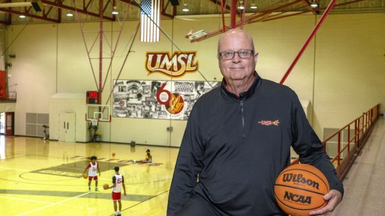 Bob Sundvold holds a basketball while standing in the Mark Twain Athletic Center with Chuck Smith Court behind him