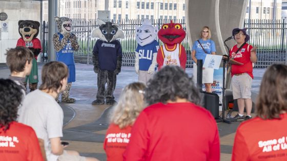 UMSL student Remy Xa speaks at a kickoff for the College Transit Challenge while mascots from area colleges stand nearby