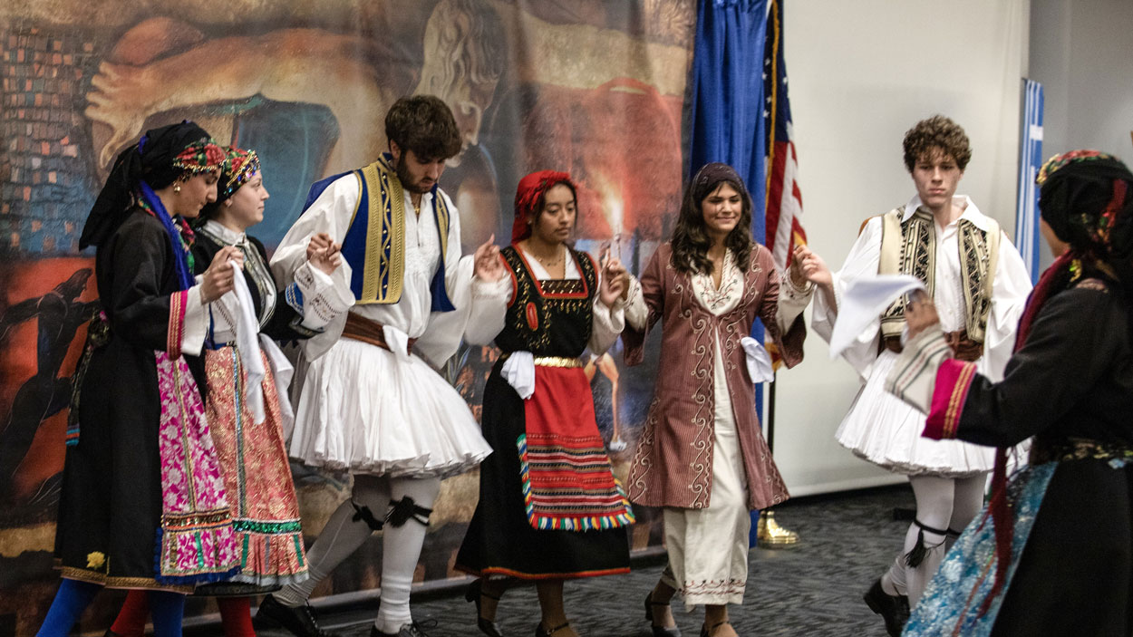 Greek dancers perform in front of a recreation of Rip Kastaris' mural "Kyklos – Circle of Glory"