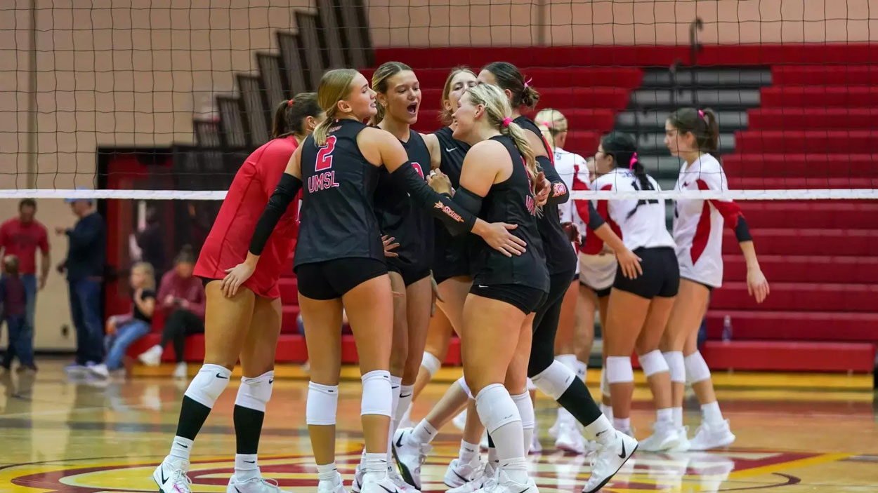 Members of the UMSL volleyball team huddle near the net as they celebrate a point