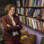 University of Missouri–St. Louis Associate Professor of History Anne Austin standing in her office with bookshelf to her left