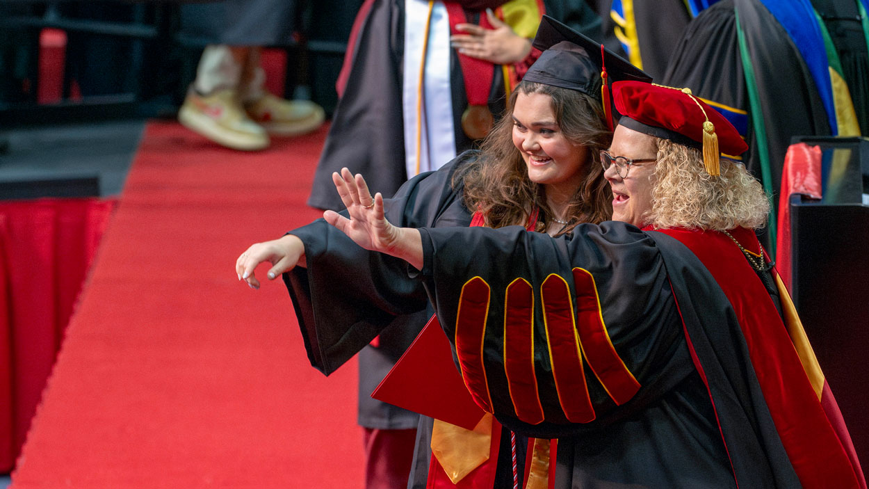 Accounting graduate Alex Paubel and Chancellor Kristin Sobolik wave to Paubel's family during commencement