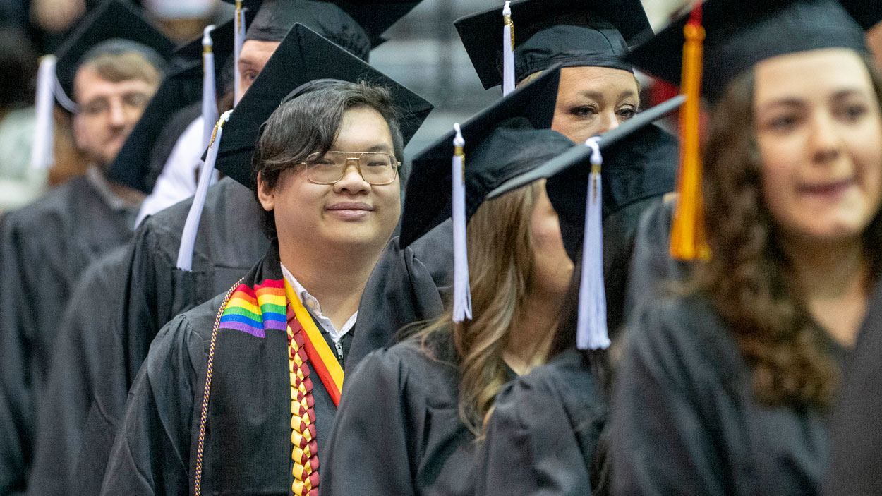 UMSL Bachelor of Arts in Communications and Pierre Laclede Honors College graduate Remy Xa, smiles as they walk into commencement ceremony.