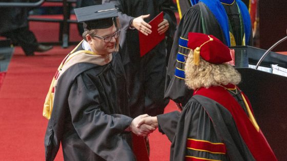 Jarad Perry shakes hands with Chancellor Kristin Sobolik on the commencement stage at the Mark Twain Athletic Center