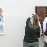 Associate Teaching Professor Michael Behle and lab technician Valerie Dratwick from the Department of Art and Design at the University of Missouri–St. Louis hang works of art from the exhibition "Hung Together" on the third floor of the Millennium Student Center
