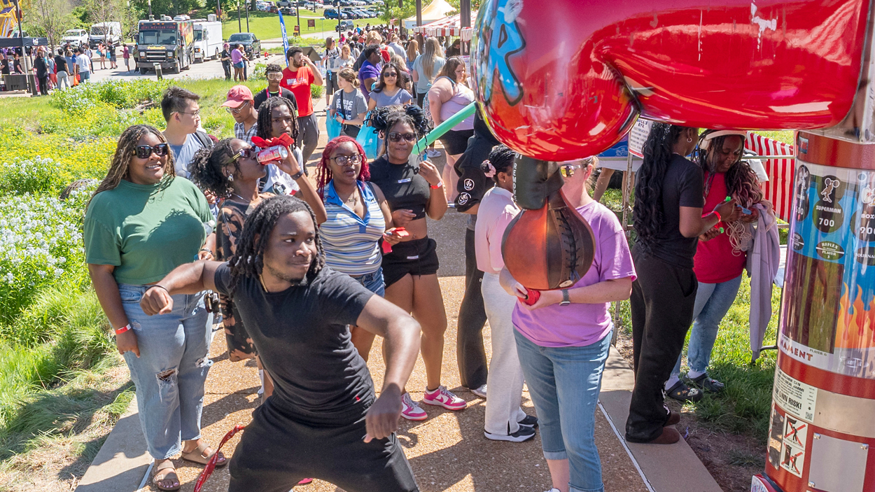 UMSL senior electrical engineering major, Clint Newry, tries out the punching bag at the Mrith festival carnival as a crowd watches. 