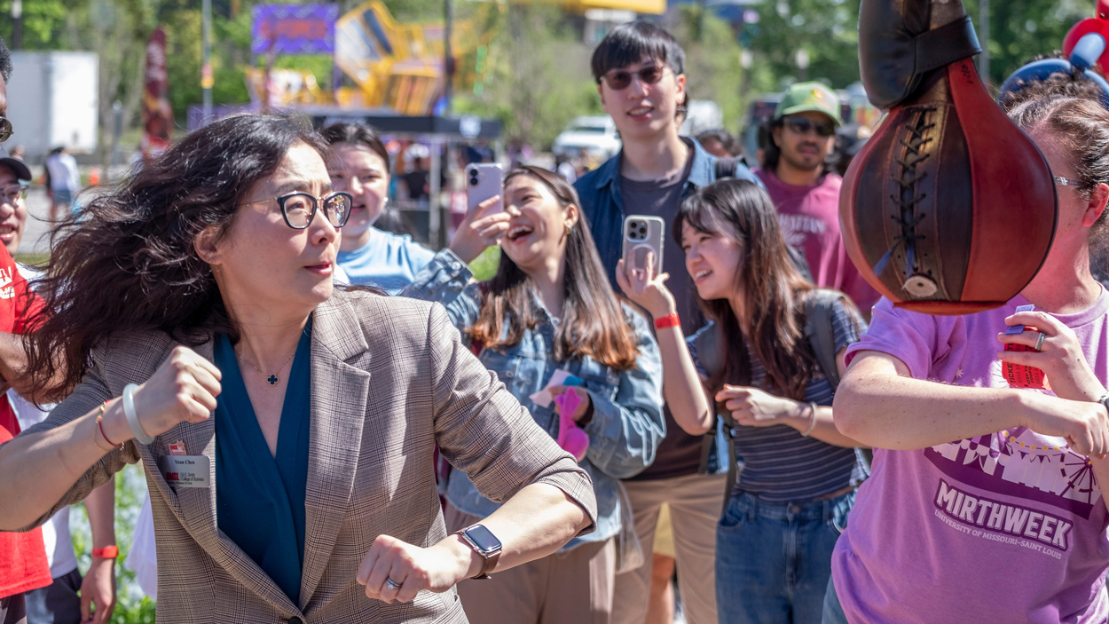 Students watch as University of Missouri–St. Louis director, business success, Yuan Chen, takes a turn at the punching game during the Mirth Week Carnival. 