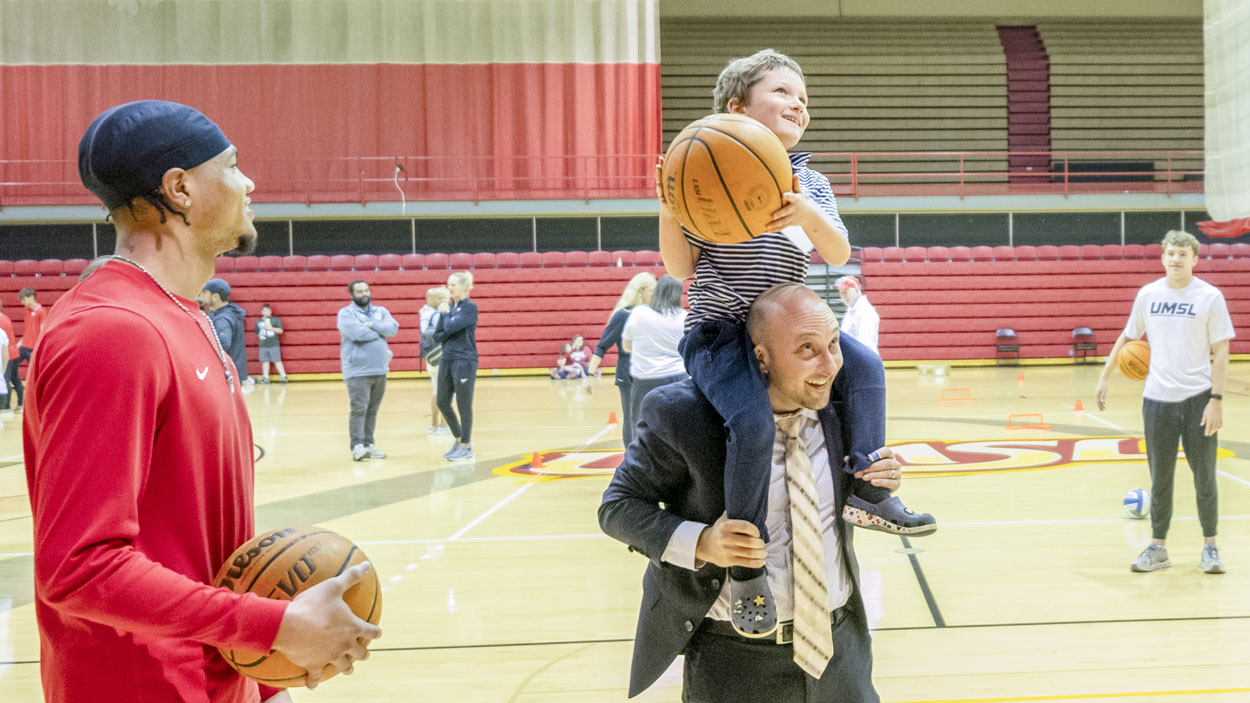 Leonid Pugachev, an assistant professor of finance, puts his son on his shoulders to help him attempt a shot at the basketball hoop at the Mark Twain Athletic Center during "Bring a Child To Work Day" on April 23